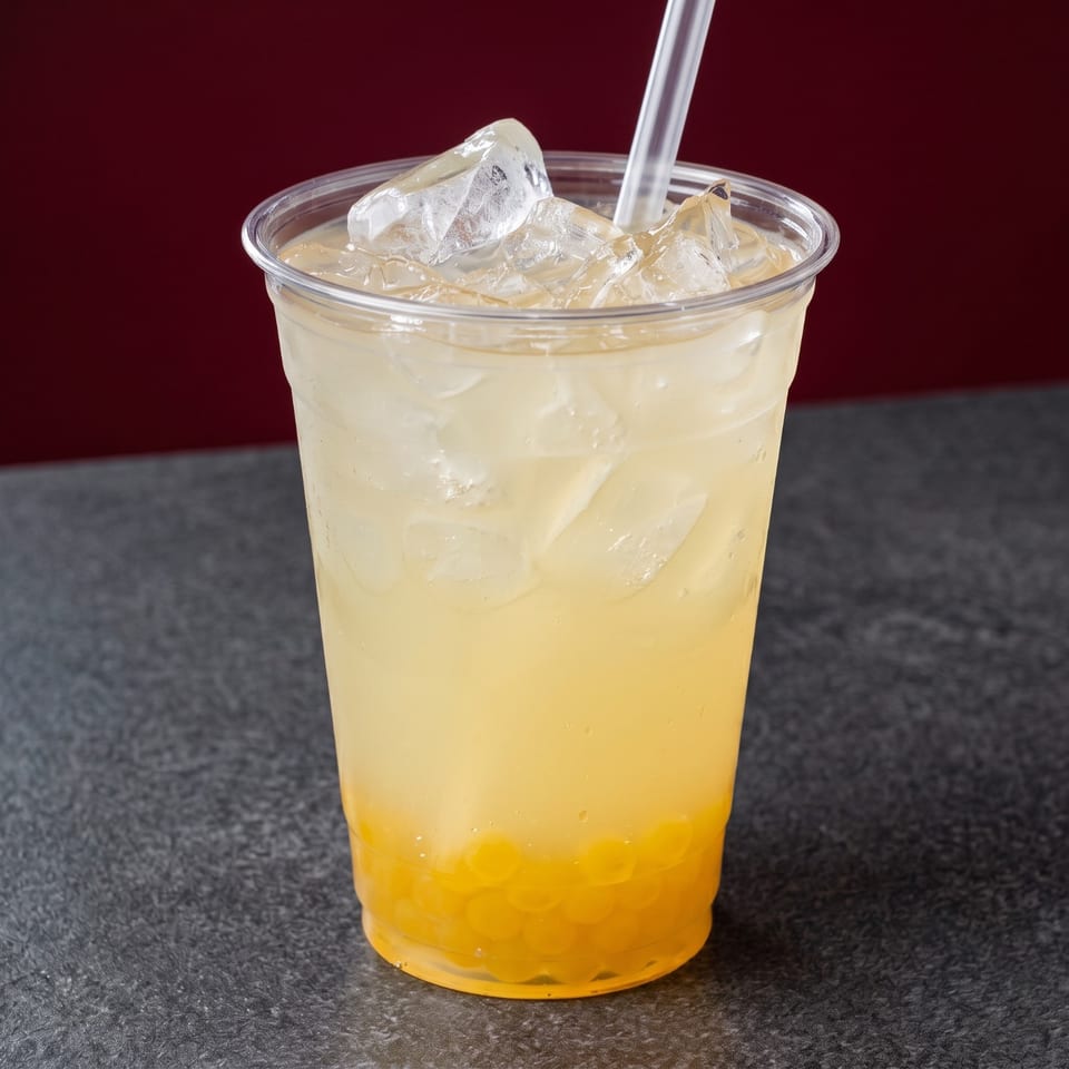 A plastic cup of iced lemonade with yellow boba pearls and a straw on a dark table.